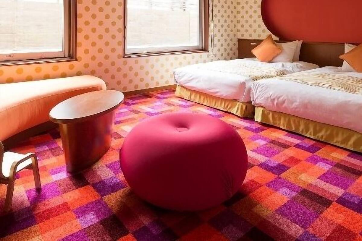 Ein Hotelzimmer mit einem Bett, einer Sitzecke, einem runden Hocker und einem gemusterten Teppich.