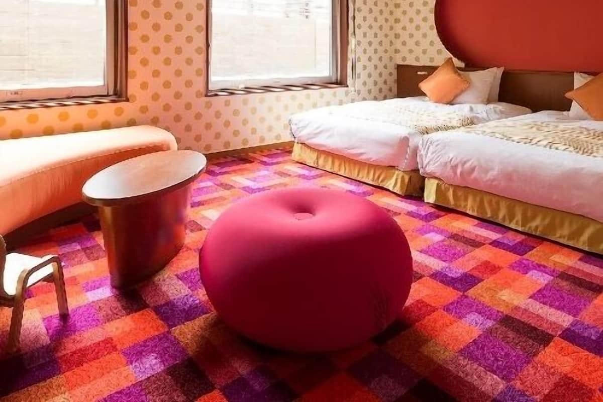 Une chambre d’hôtel comprenant un lit, un coin salon, un pouf rond et une moquette à motifs.
