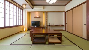 A traditional Japanese room with tatami flooring, a low table with cushions, a television, and sliding doors. - Yaizu Grand Hotel (Yaizu)