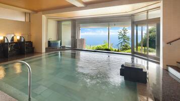 An indoor swimming pool with a view of the ocean, a sauna area, and a staircase leading to an outdoor area.