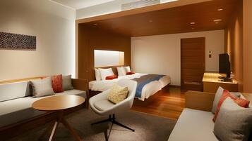 A modern hotel room with a sofa, a round table, a bed with multiple pillows, and a television.