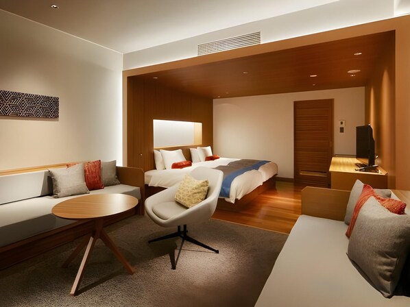 A modern hotel room with a sofa, a round table, a bed with multiple pillows, and a television. - Yaizu Grand Hotel (Yaizu)