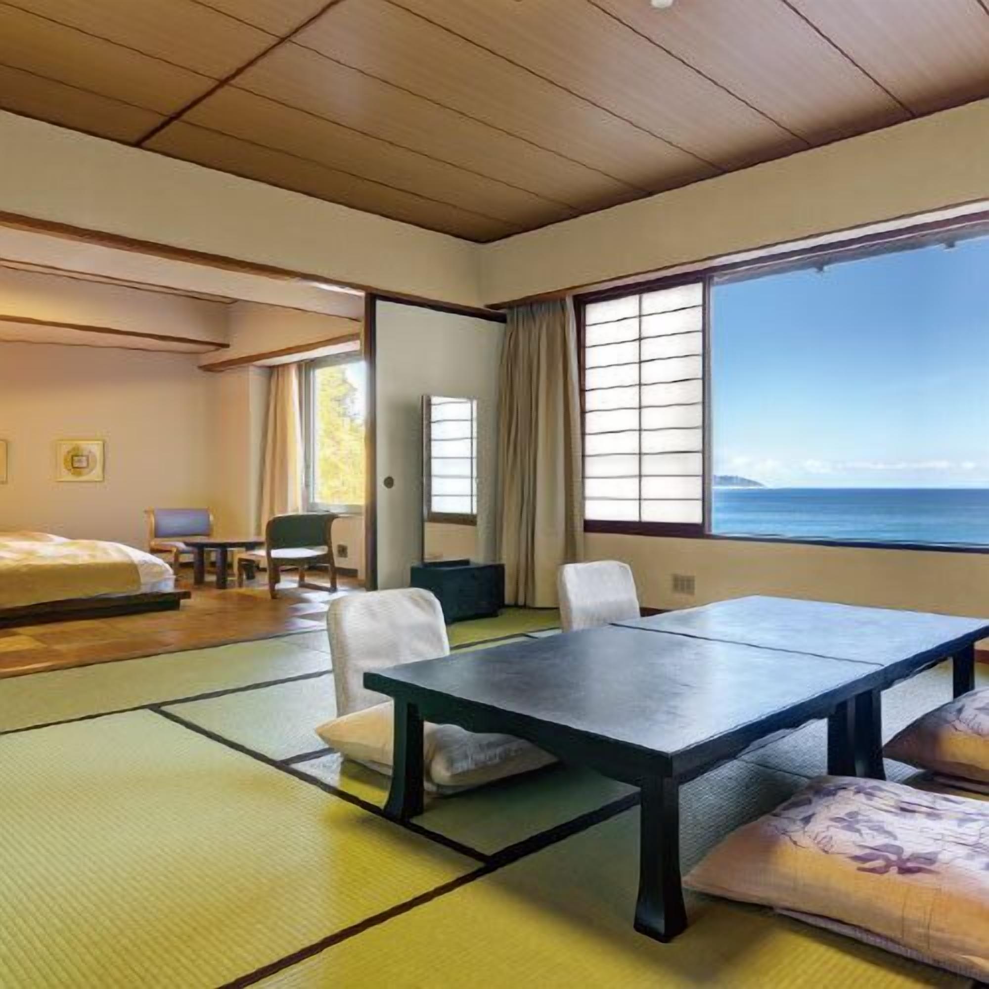 Une pièce avec des tatamis, un lit, une table, des chaises, un bureau et une vue sur la mer.