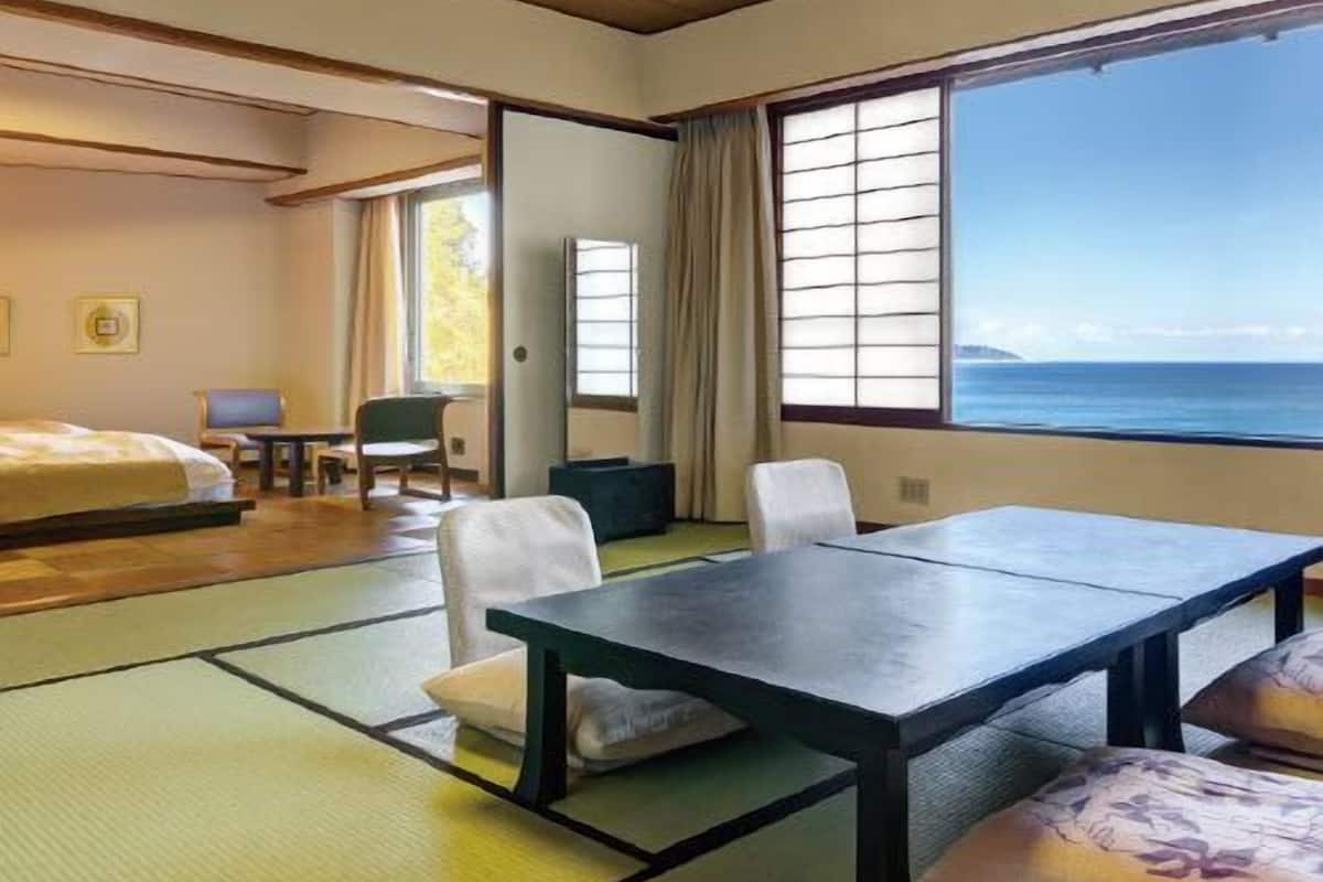 Ein Zimmer mit Tatami-Matten, einem Bett, einem Tisch, Stühlen, einem Schreibtisch und Meerblick.