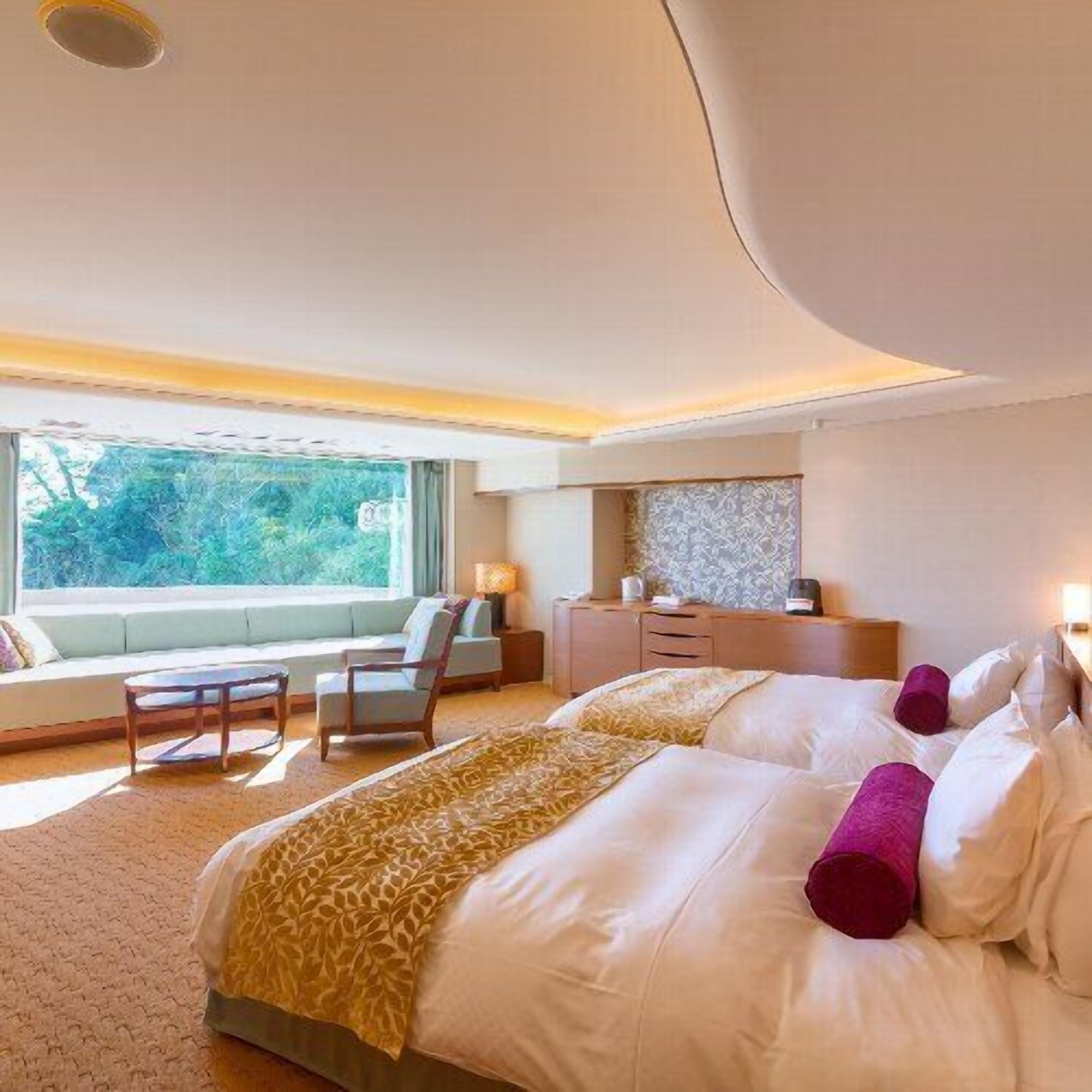 Une chambre d’hôtel avec un grand lit, un canapé, un bureau et une fenêtre donnant sur un paysage verdoyant.