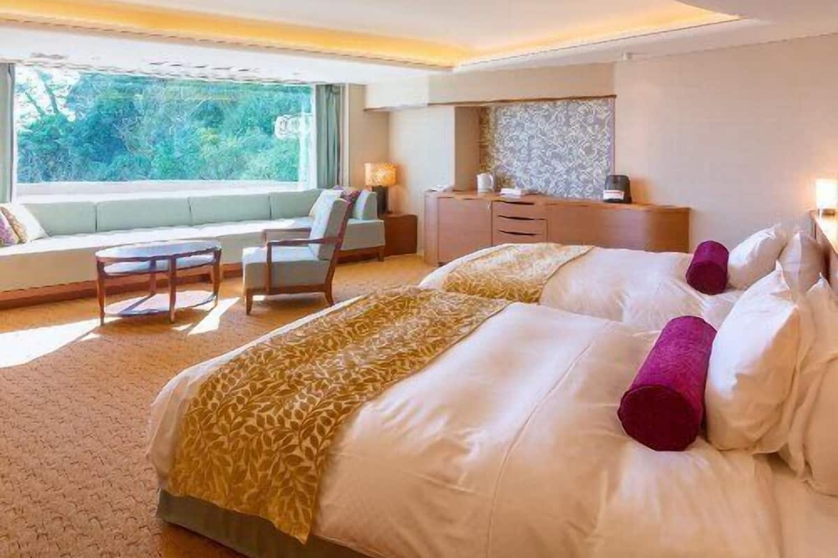 Ein Hotelzimmer mit einem großen Bett, einer Sitzecke, einem Schreibtisch und einem Fenster mit Blick auf Grünflächen.