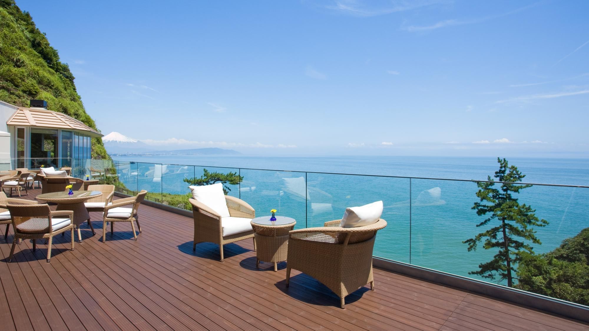 A wooden deck with wicker furniture and glass balustrades overlooking a body of water.