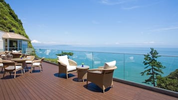 A wooden deck with wicker furniture and glass balustrades overlooking a body of water.