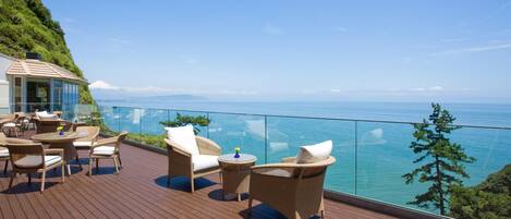 A wooden deck with wicker furniture and glass balustrades overlooking a body of water.