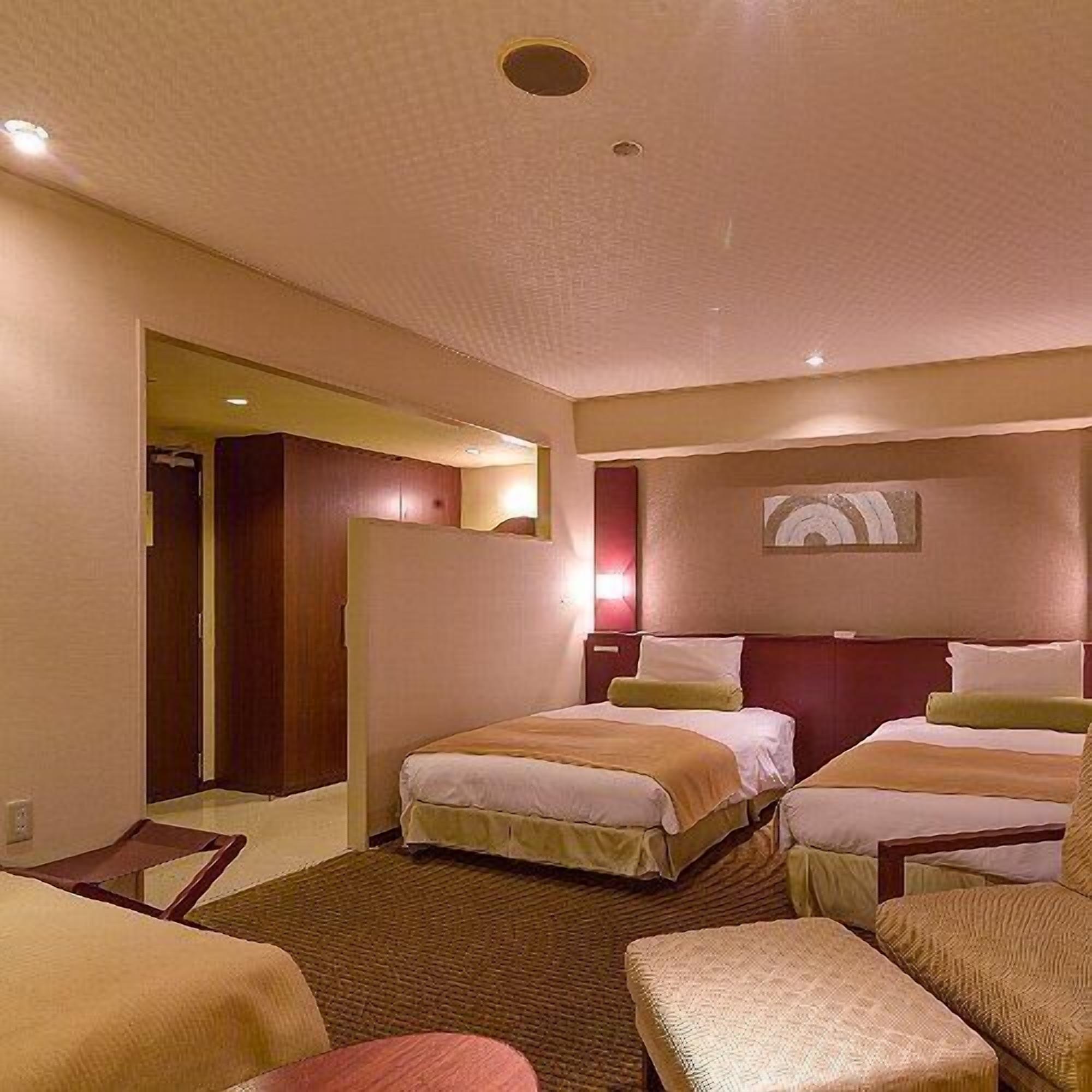Una camera d'albergo con due letti, un'area salotto e un ingresso che conduce a un'altra stanza.