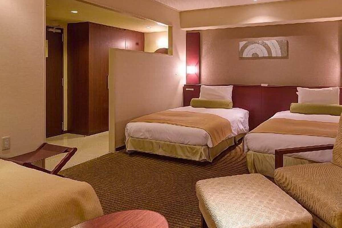 Ein Hotelzimmer mit zwei Betten, einer Sitzecke und einer Tür zu einem weiteren Raum.
