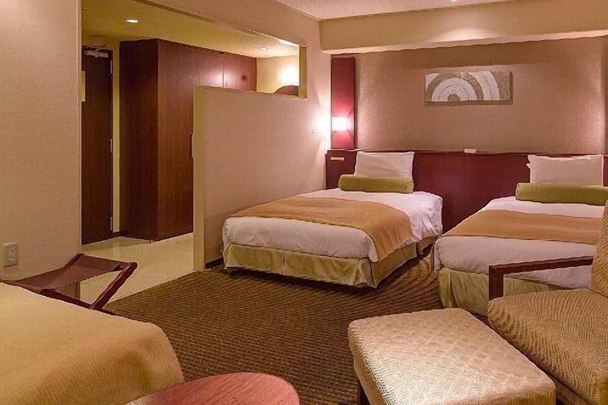 Una camera d'albergo con due letti, un'area salotto e un ingresso che conduce a un'altra stanza.