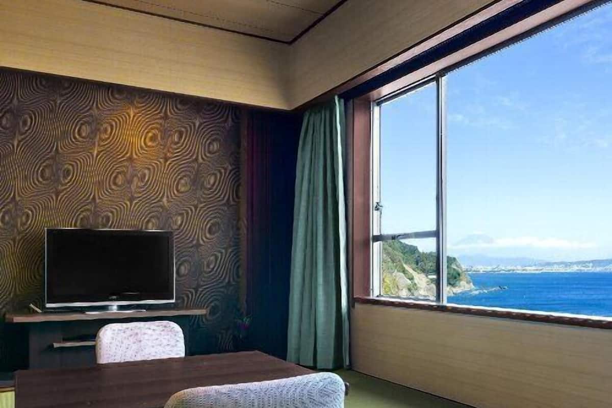 Ein Zimmer mit Fernseher, Tisch, Stuhl und einem großen Fenster mit Meerblick.