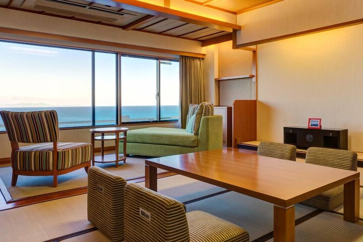 Ein Hotelzimmer mit Tatami-Boden, einer Couch, einem Sessel, einem Tisch und Meerblick.