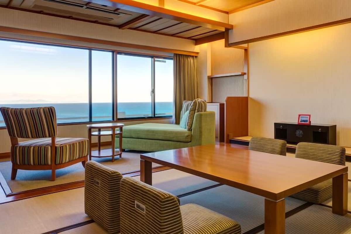 A hotel room with tatami flooring, a sofa, a chair, a table, and a view of the ocean.