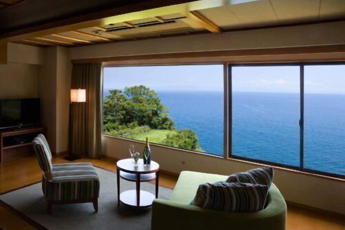 A room with a large window, a sofa, a chair, a small table, and a television.