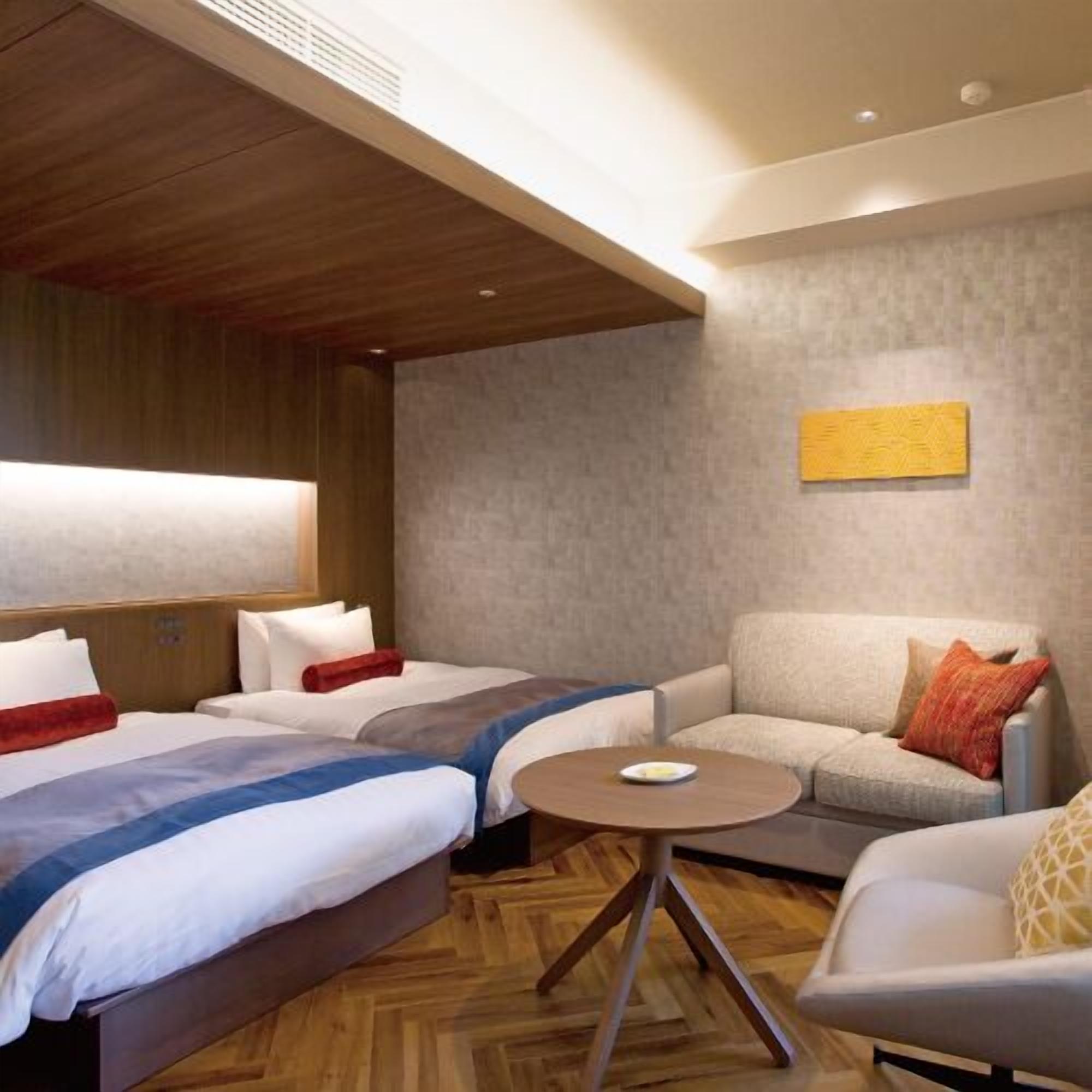 Camera d'albergo con due letti, una poltrona, un tavolino rotondo e un quadro appeso al muro.