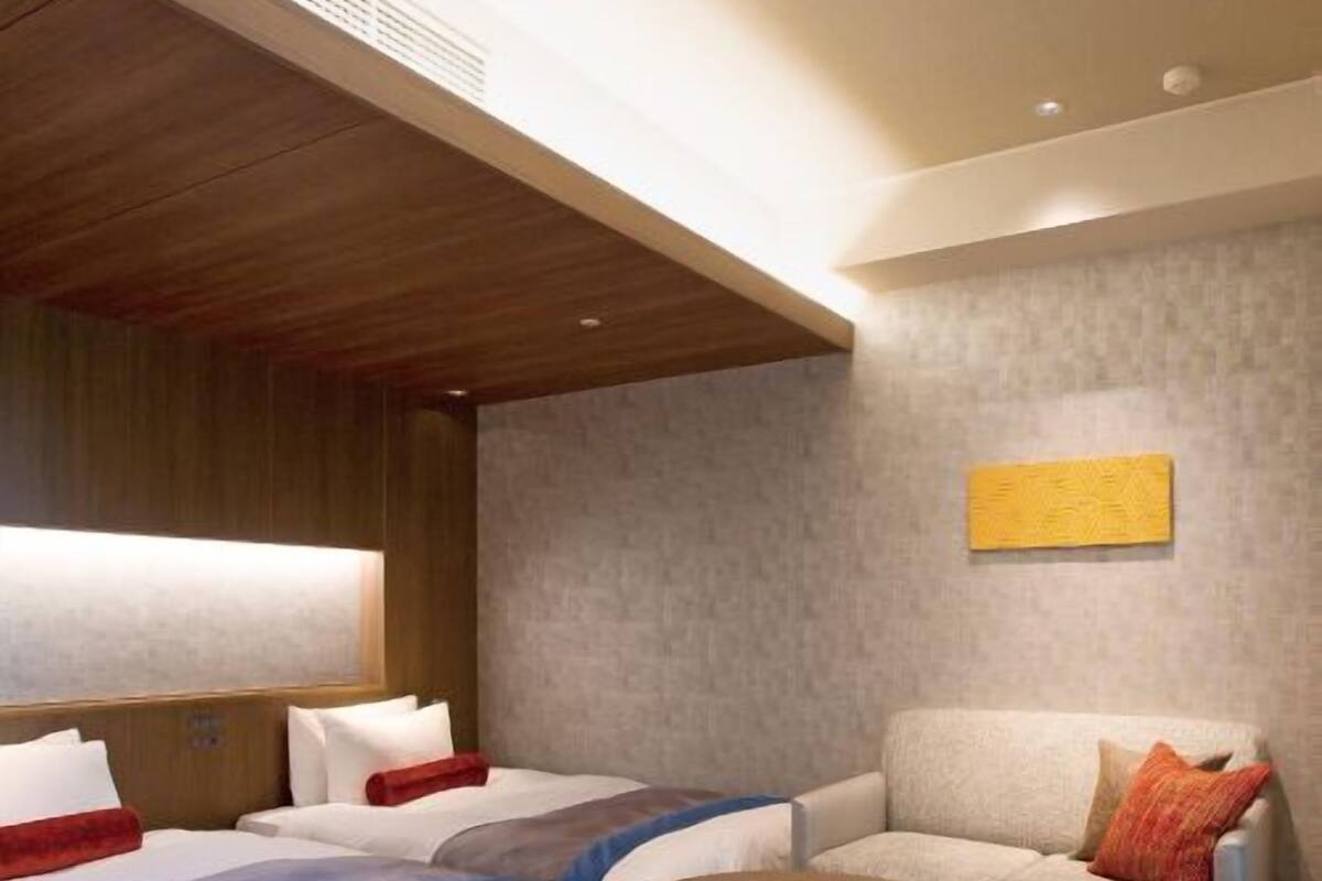 Camera d'albergo con due letti, una poltrona, un tavolino rotondo e un quadro appeso al muro.