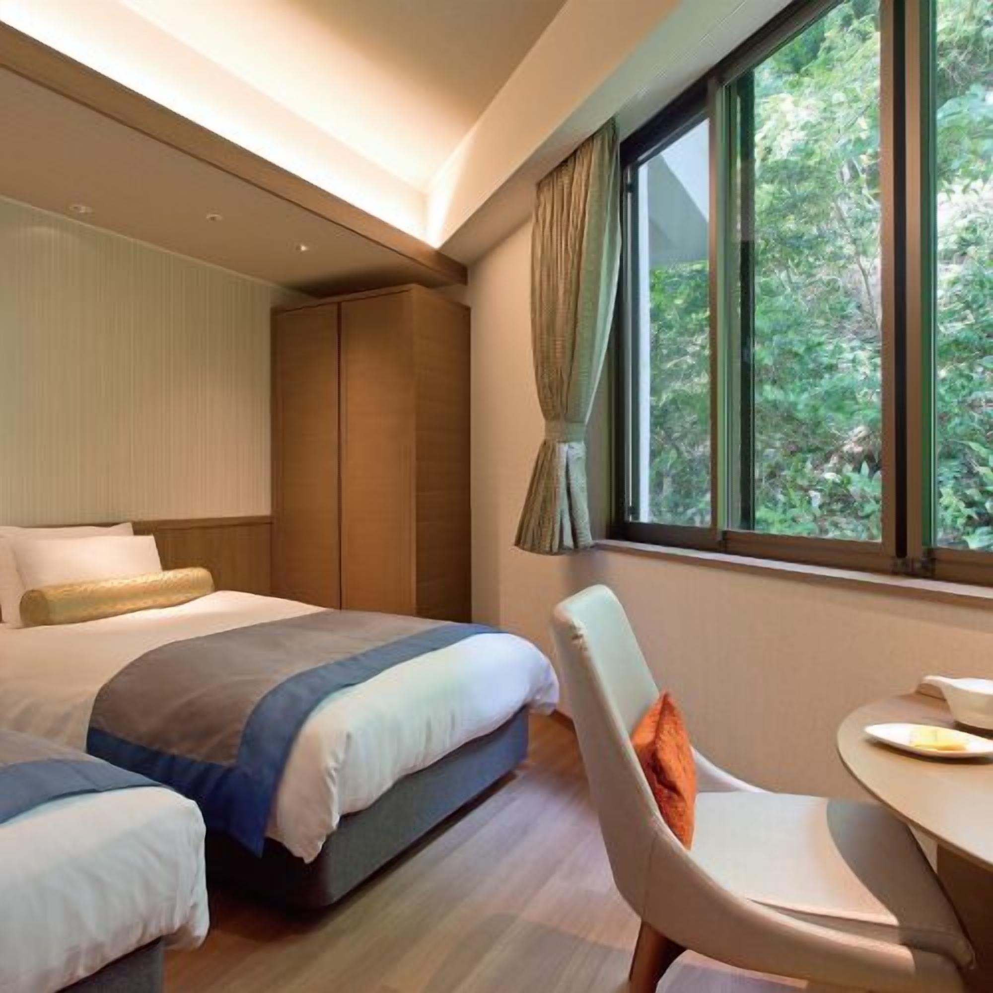 Une chambre d’hôtel avec un lit, une chaise, une table et une fenêtre donnant sur un paysage verdoyant.