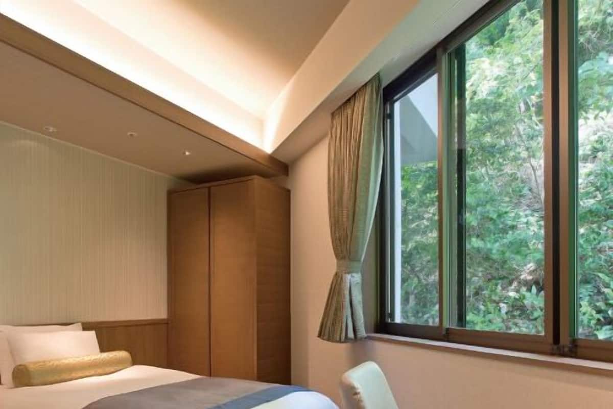 Ein Hotelzimmer mit Bett, Stuhl, Tisch und einem Fenster mit Blick auf Grünflächen.
