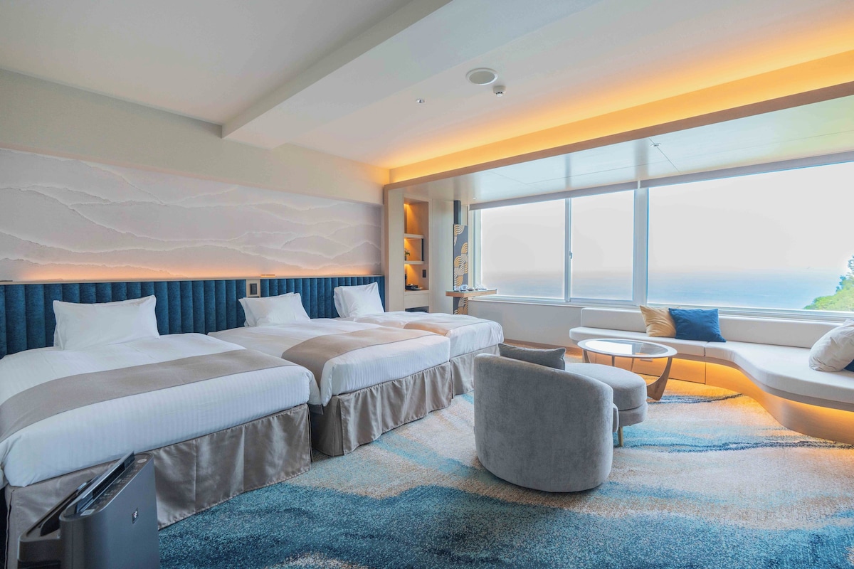 Une chambre d’hôtel avec deux lits, un canapé, une petite table et une vue sur l’océan.
