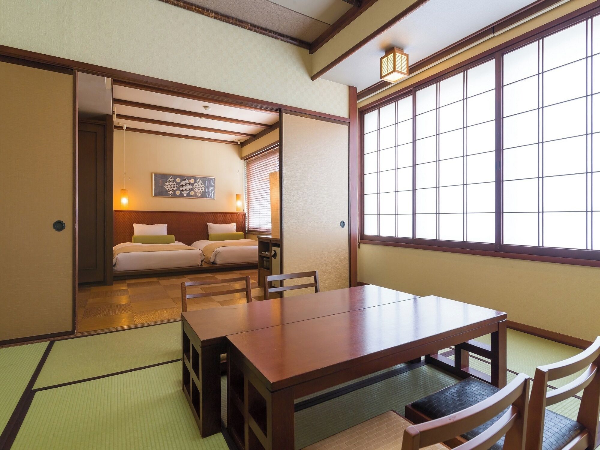 Une pièce de style japonais traditionnel, avec un sol recouvert de tatamis, une petite table en bois et une porte coulissante donnant accès à une chambre à coucher équipée de deux lits.