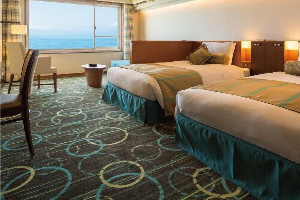 Ein Hotelzimmer mit zwei Betten, einem Schreibtisch, einem Stuhl und Blick auf den Ozean.