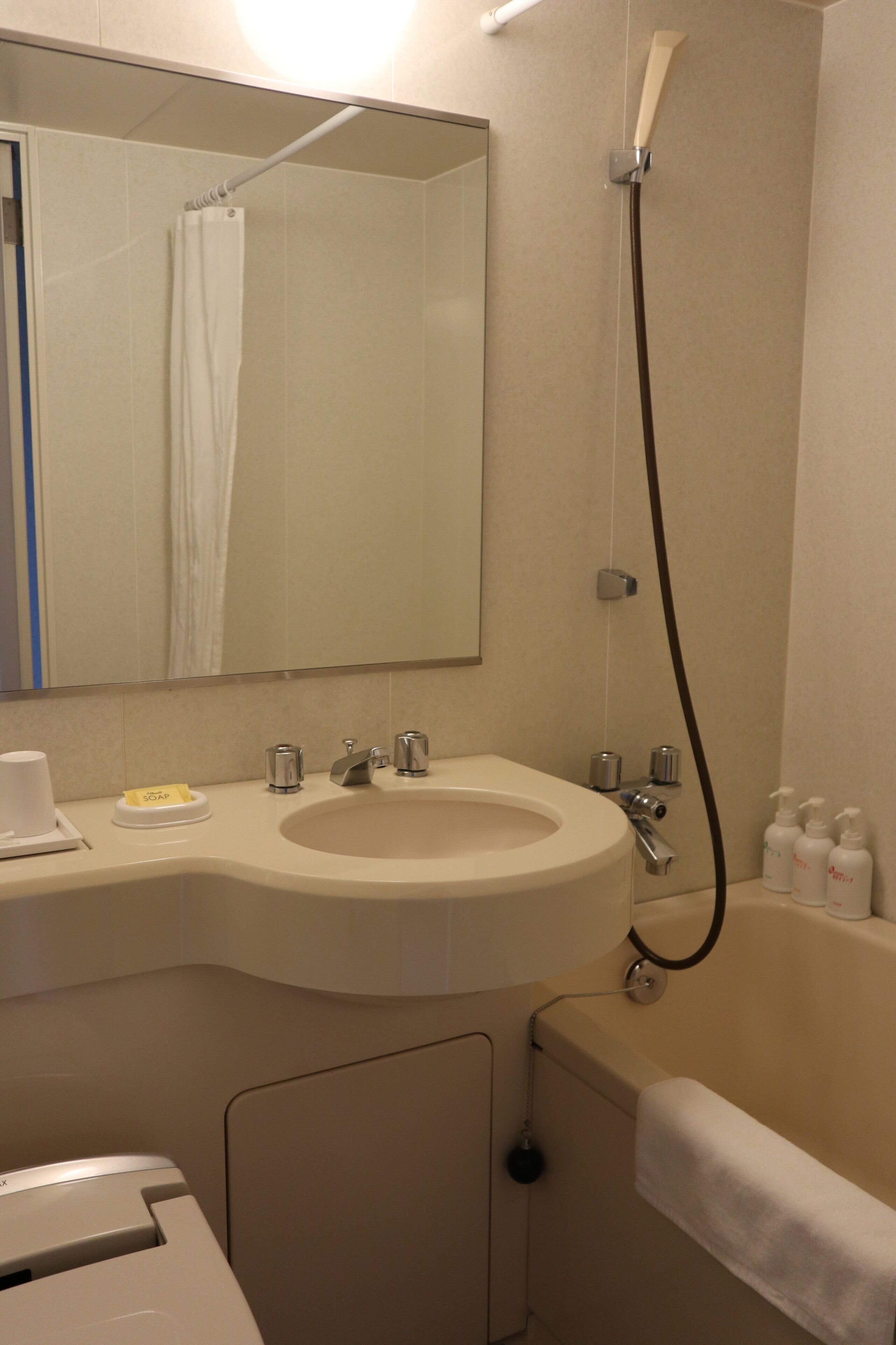 A bathroom with a sink, mirror, shower, and a towel rack.