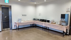 A conference room with a long table, multiple electrical outlets, a fire exit, and a coffee machine. - Plaza Hotel Sanda (Sanda)