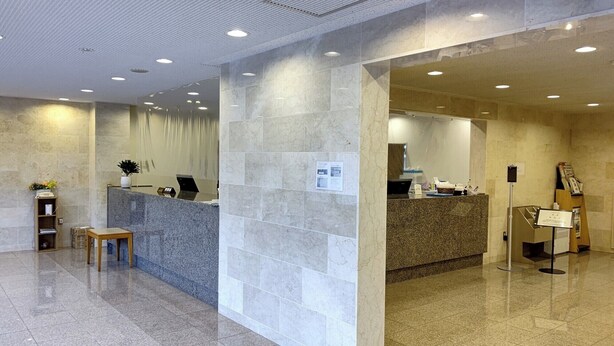 A reception area with a marble counter, a small wooden table, and a potted plant. - Plaza Hotel Sanda (Sanda)