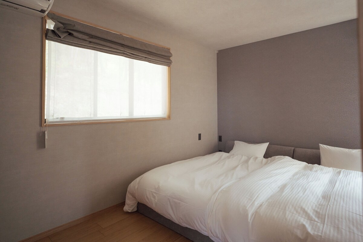 Ein Schlafzimmer mit einem Einzelbett, einem Fenster mit Vorhängen und einer schlichten Wand.