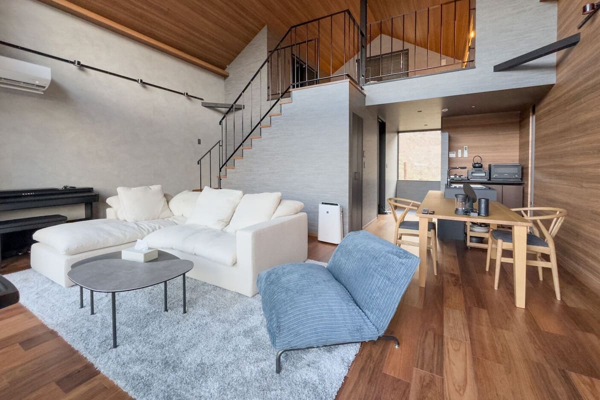 A modern living room with a sofa, coffee table, and a dining area with chairs and a table.