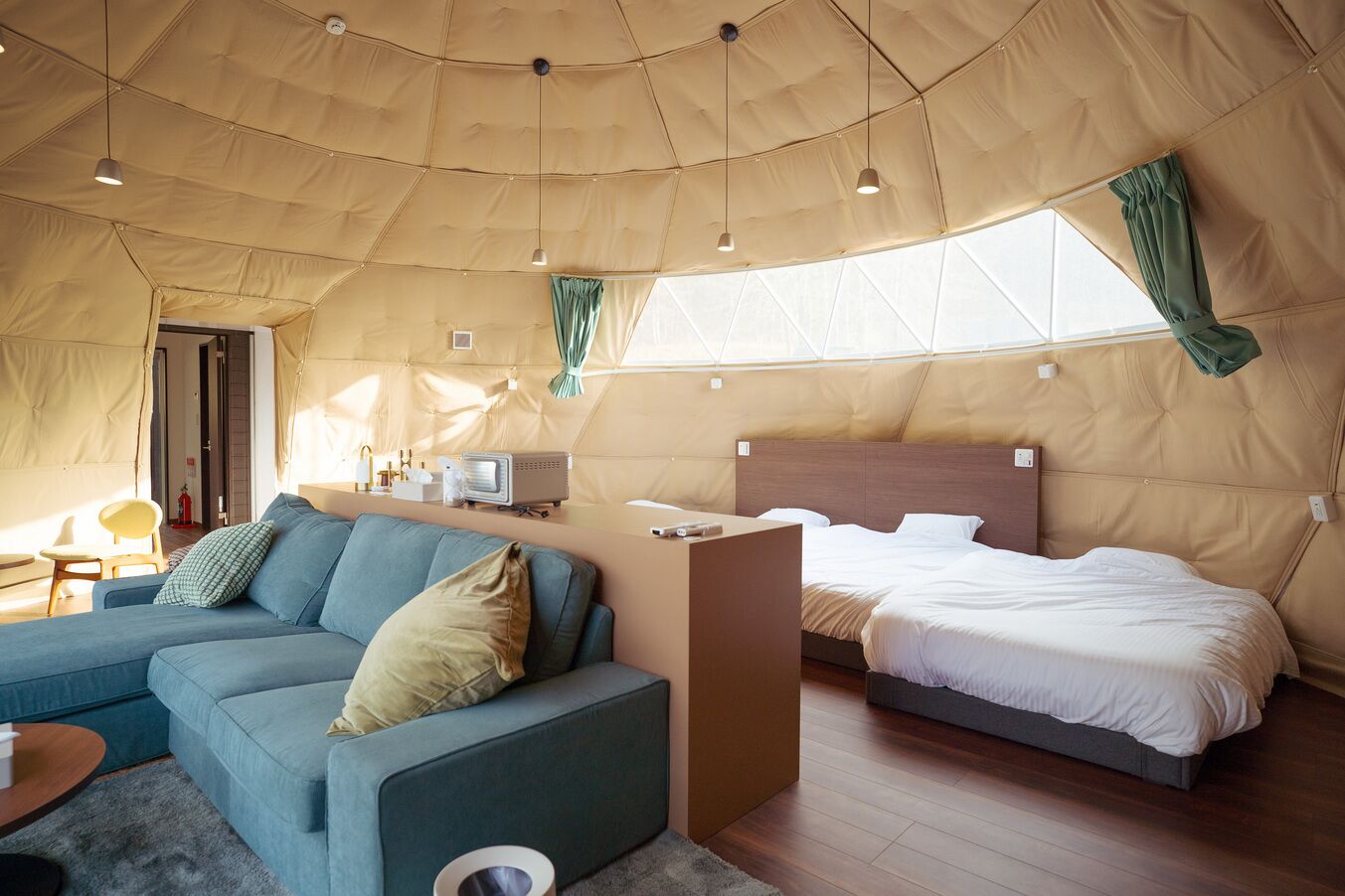 Een tent-achtige kamer met een slaapbank, een bed, een tafeltje en een televisie.