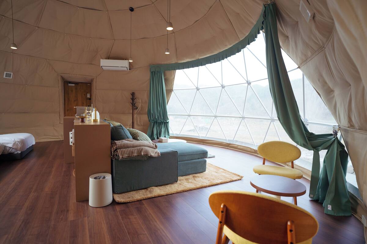 Une pièce aménagée comme un salon, avec un canapé, des fauteuils, une petite table et un plancher en bois.