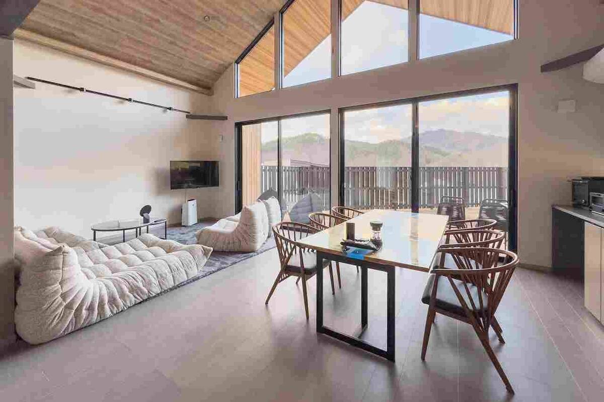 Un vaste espace de vie comprenant une grande table à manger, des sièges confortables et une vue dégagée grâce à de grandes fenêtres.