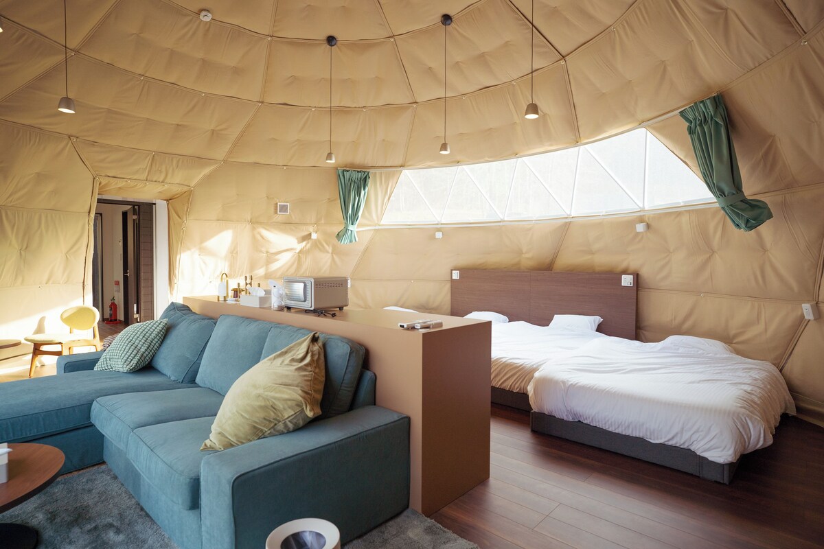 Eine Zelthütte mit einer Couch, einem Bett, einem kleinen Tisch und einem Fernseher.