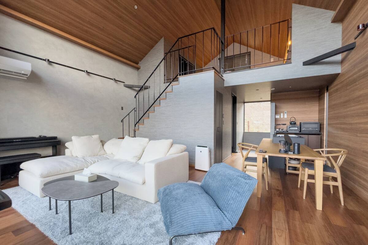 Un salon moderne avec un canapé, une table basse et un fauteuil bleu. Un escalier mène à un niveau supérieur.