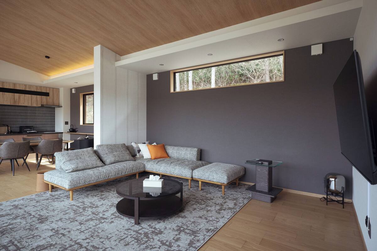 Un salon moderne avec un canapé d’angle, une table basse et un téléviseur fixé au mur.
