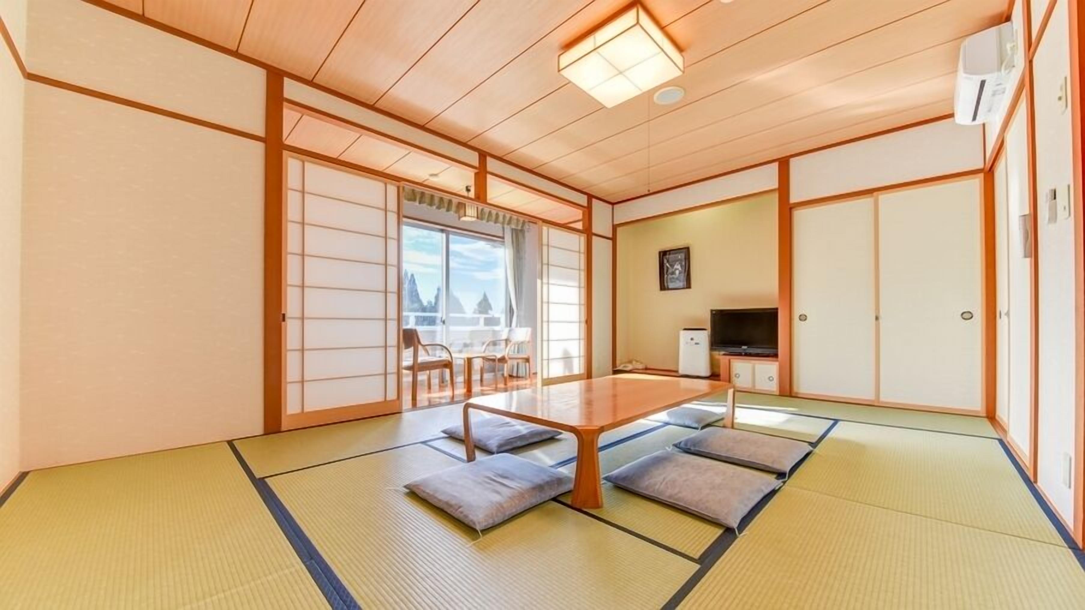 Una tradizionale stanza in stile giapponese, con pavimento in tatami, un tavolino basso, cuscini, porte scorrevoli e un televisore.