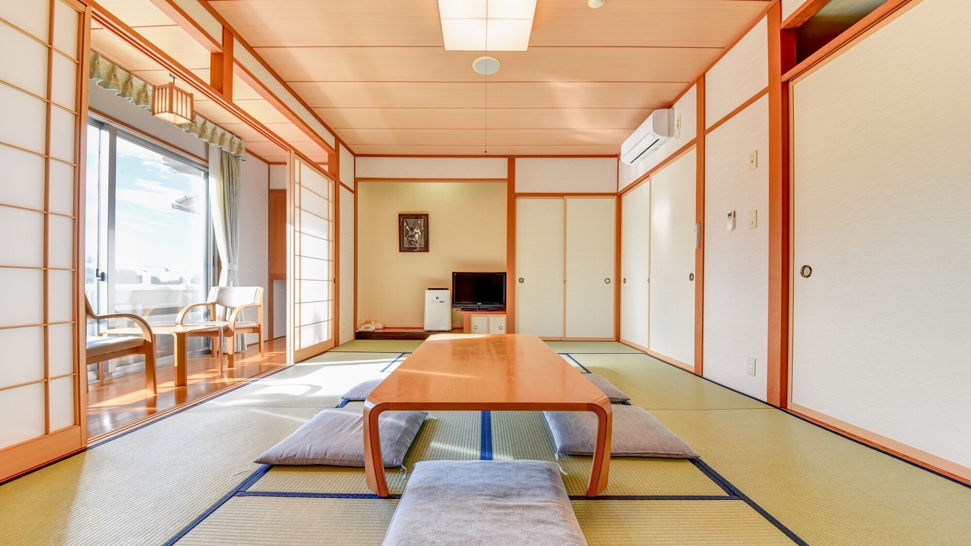 Ein traditioneller japanischer Raum mit Tatami-Böden, einem niedrigen Holztisch, Schiebetüren und einem Fernseher.