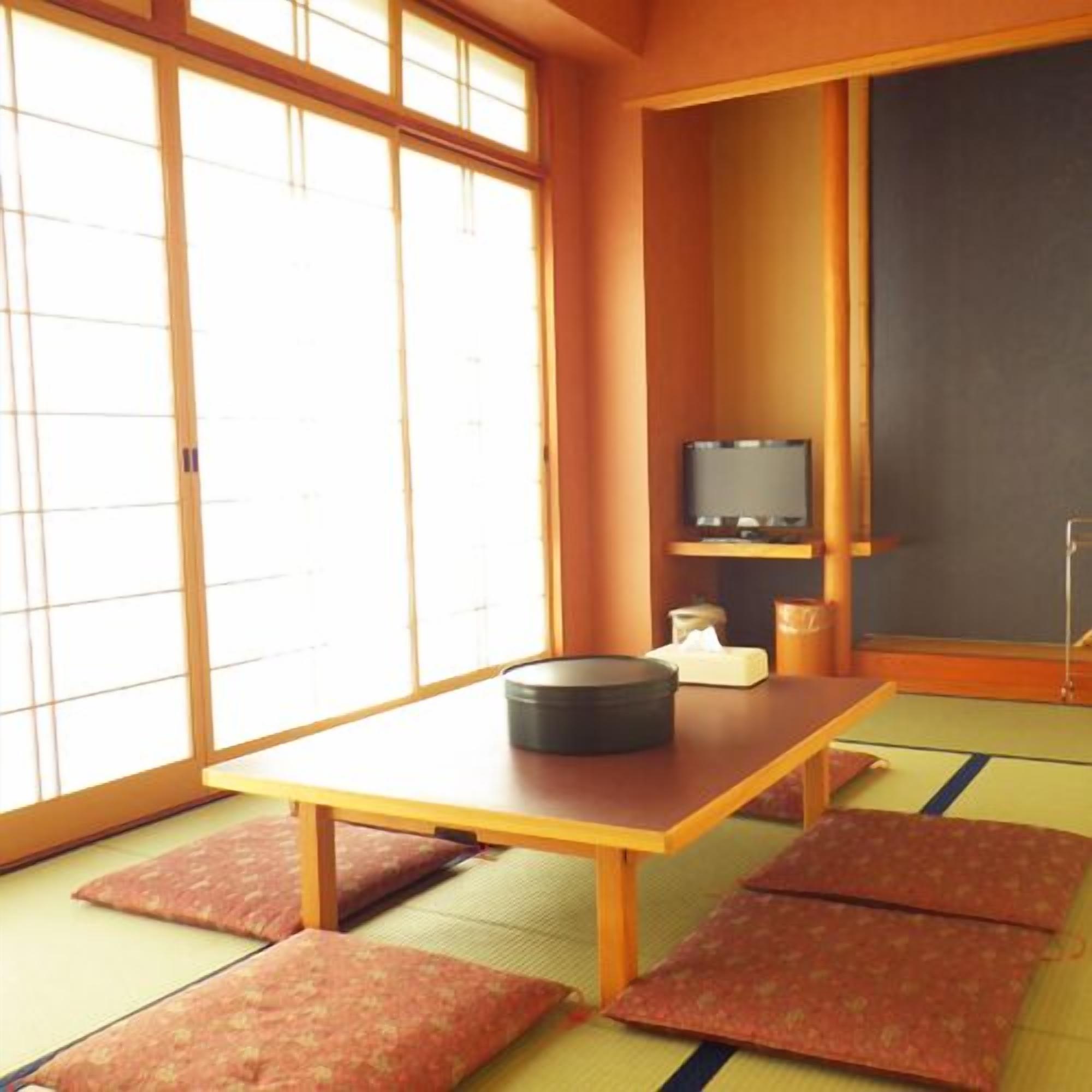 Ein Raum mit Tatami-Matten, einem Tatami-Tisch, Kissen, einem Fernseher und einer Kreidetafel.