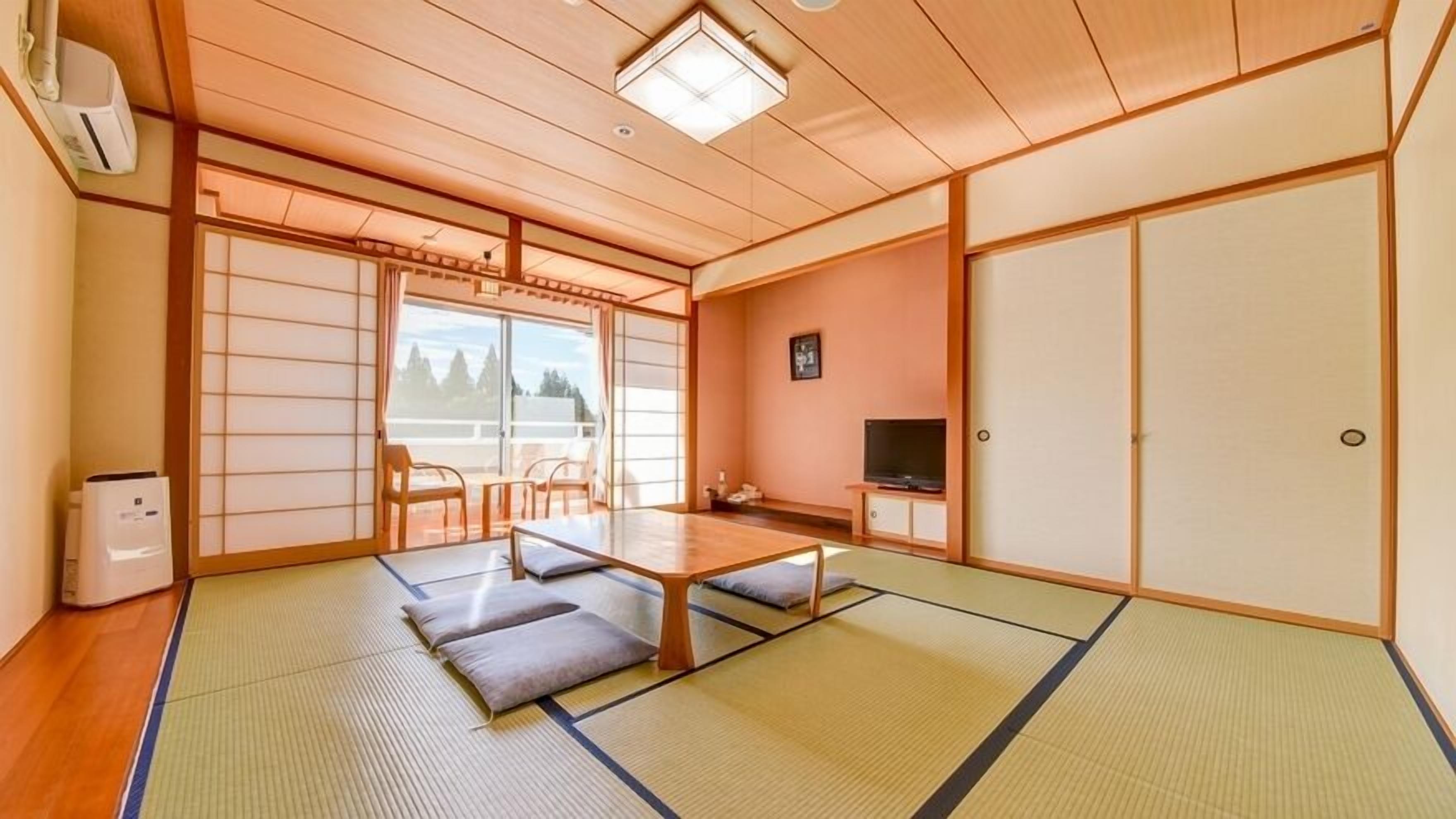 Una tradizionale stanza giapponese con pavimento in tatami, un tavolino con cuscini, porte scorrevoli e un televisore.