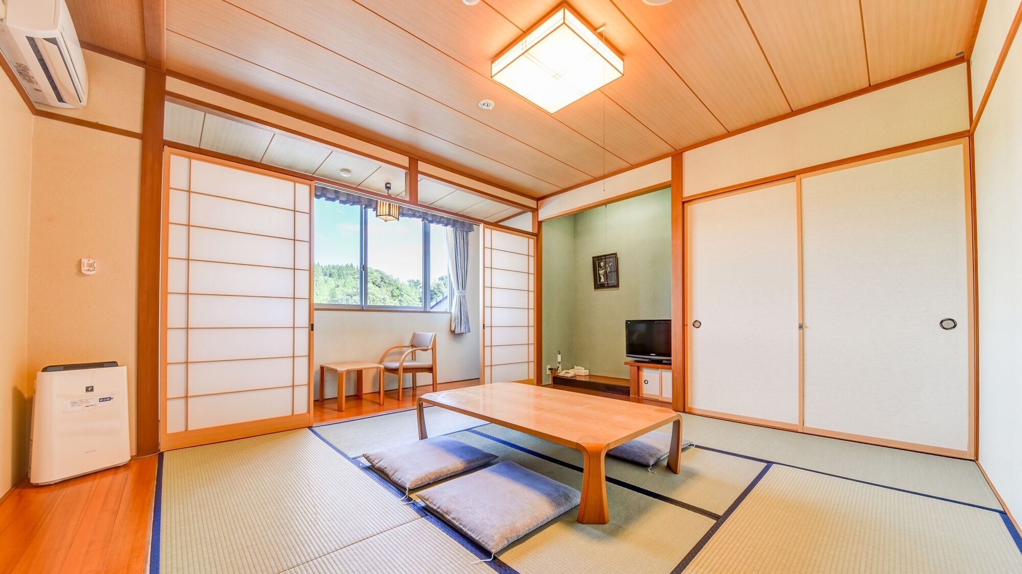 Ein traditioneller japanischer Raum mit Tatami-Bodenbelag, einem niedrigen Tisch, Schiebetüren und einem Fernseher.