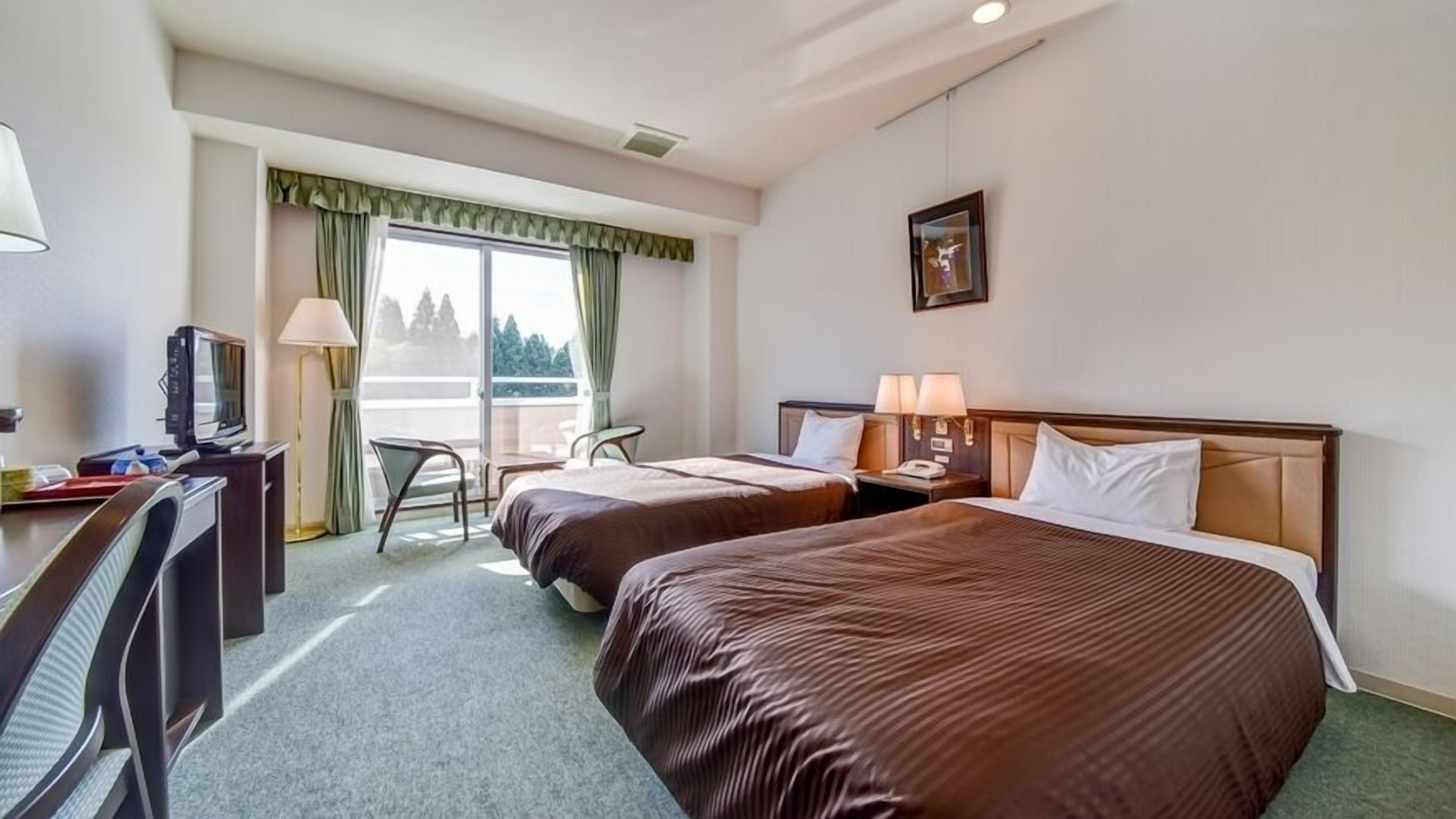 Una camera d'albergo con due letti, una scrivania con televisore, una sedia e un balcone con vista.