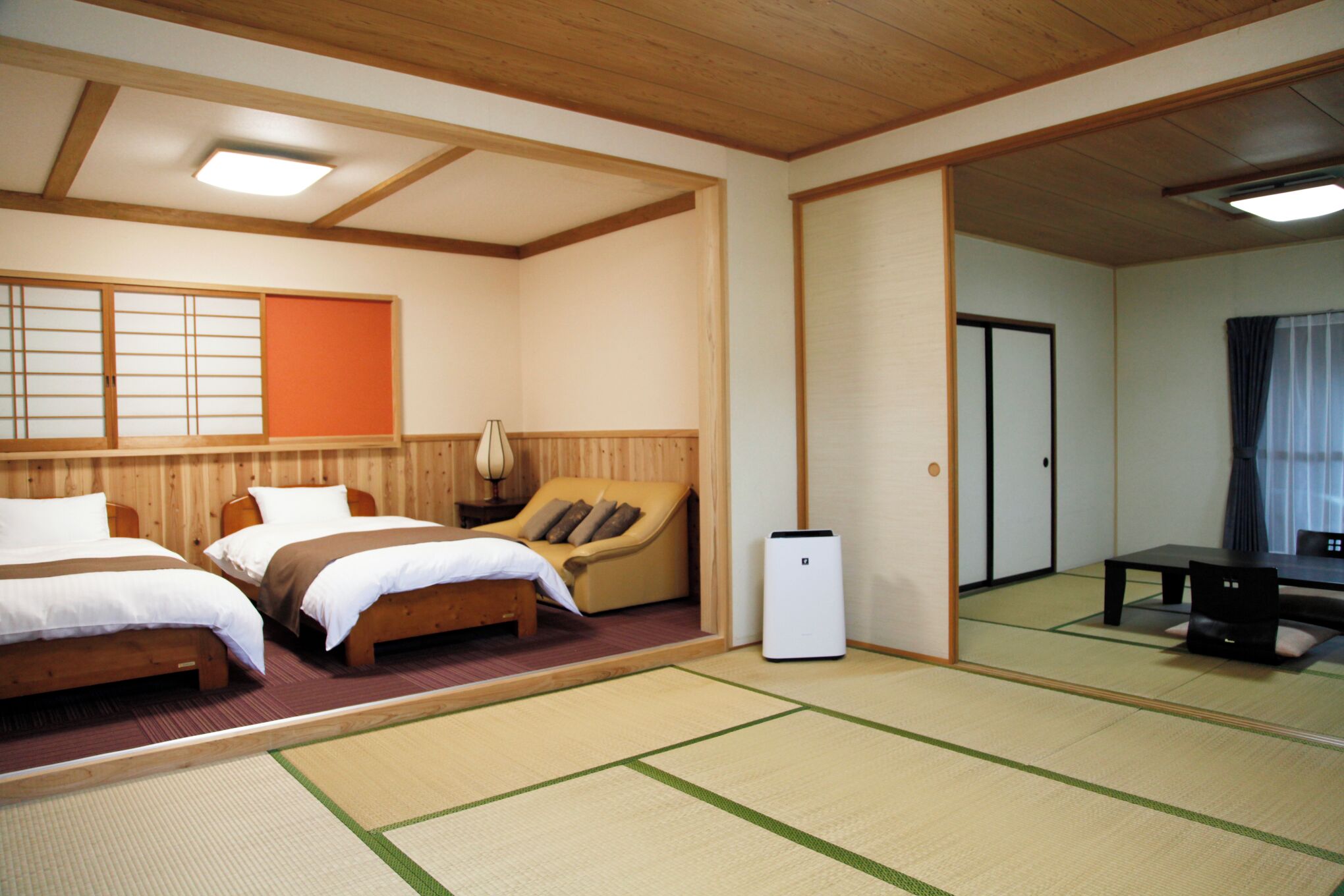 A traditional Japanese-style room with tatami flooring, two beds, a sofa, a table, and a television.