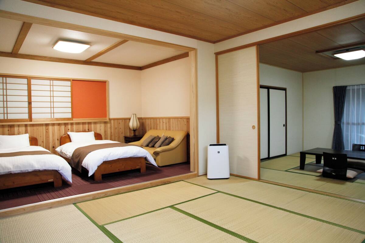 Ein traditionell eingerichteter japanischer Raum mit Tatami-Böden, zwei Betten, einem Sofa, einem Tisch und einem Fernseher.
