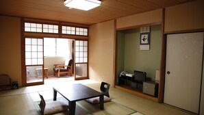 A traditional Japanese room with tatami flooring, a low table, chairs, a sliding door, and a small desk with a telephone and a computer. - Hirayama Onsen Okuyamaga Onsen Ryokan (Yamaga)