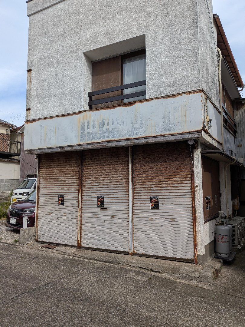 Um prédio de dois andares com uma porta de garagem fechada e uma pequena janela no andar de cima.