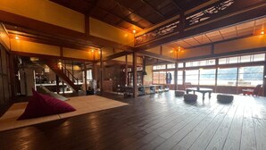 A spacious room with wooden flooring, a large window offering a view, and a staircase leading to another level. - Kominka Sent (Otoyo)