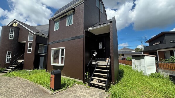 A two-story residential building with a staircase leading to the entrance, a mailbox, and a grassy area in front. - Guesthouse Towadakan (Utsunomiya)